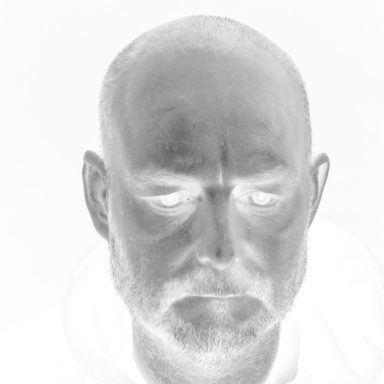 A close-up of a person’s face with a negative image effect, featuring a bald head and beard.